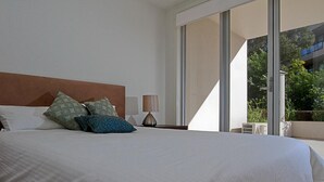 Ein Schlafzimmer mit einem großen Bett, einem Nachttisch mit Lampe und einer Glasschiebetür, die zu einem Außenbereich führt.