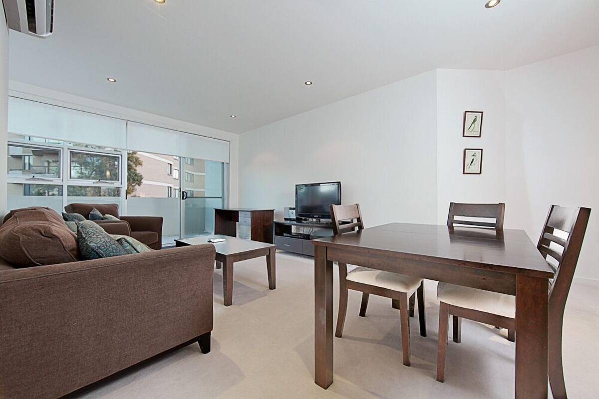 Un salon moderne comprenant un canapé, une table basse, un téléviseur et une table à manger avec des chaises.