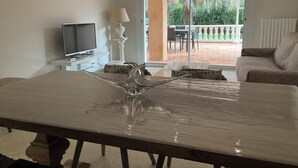 A living room with a marble table, a television, and a lamp. There is a sliding glass door leading to an outdoor area with a patio and chairs. - Pool + 10 min walk to the beach (Saint-Raphaël)