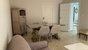 A living room with a beige sofa, a dining table with chairs, a white door, and a small wooden cabinet. - Pool + 10 min walk to the beach (Saint-Raphaël)