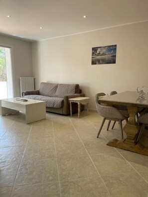 A modern living room with a sofa, a coffee table, a dining table with chairs, and a radiator.