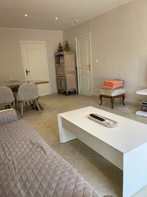 A modern bedroom with a bed, a white bedside table, a chair, a small table with a remote control, and a cabinet.