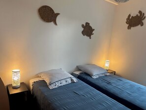 A bedroom with two beds, each with a striped pillow and a small table with a lamp.