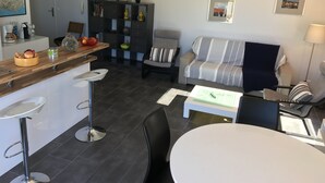 Une cuisine moderne avec un plan de travail en bois, un coin repas avec une table et des chaises blanches, un canapé à rayures et une petite bibliothèque.