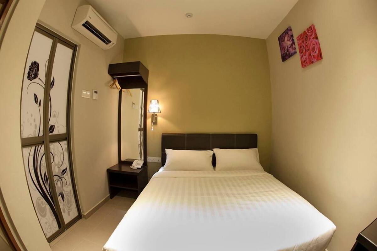 A hotel room with a bed, a nightstand, a lamp, and a wall-mounted air conditioner.