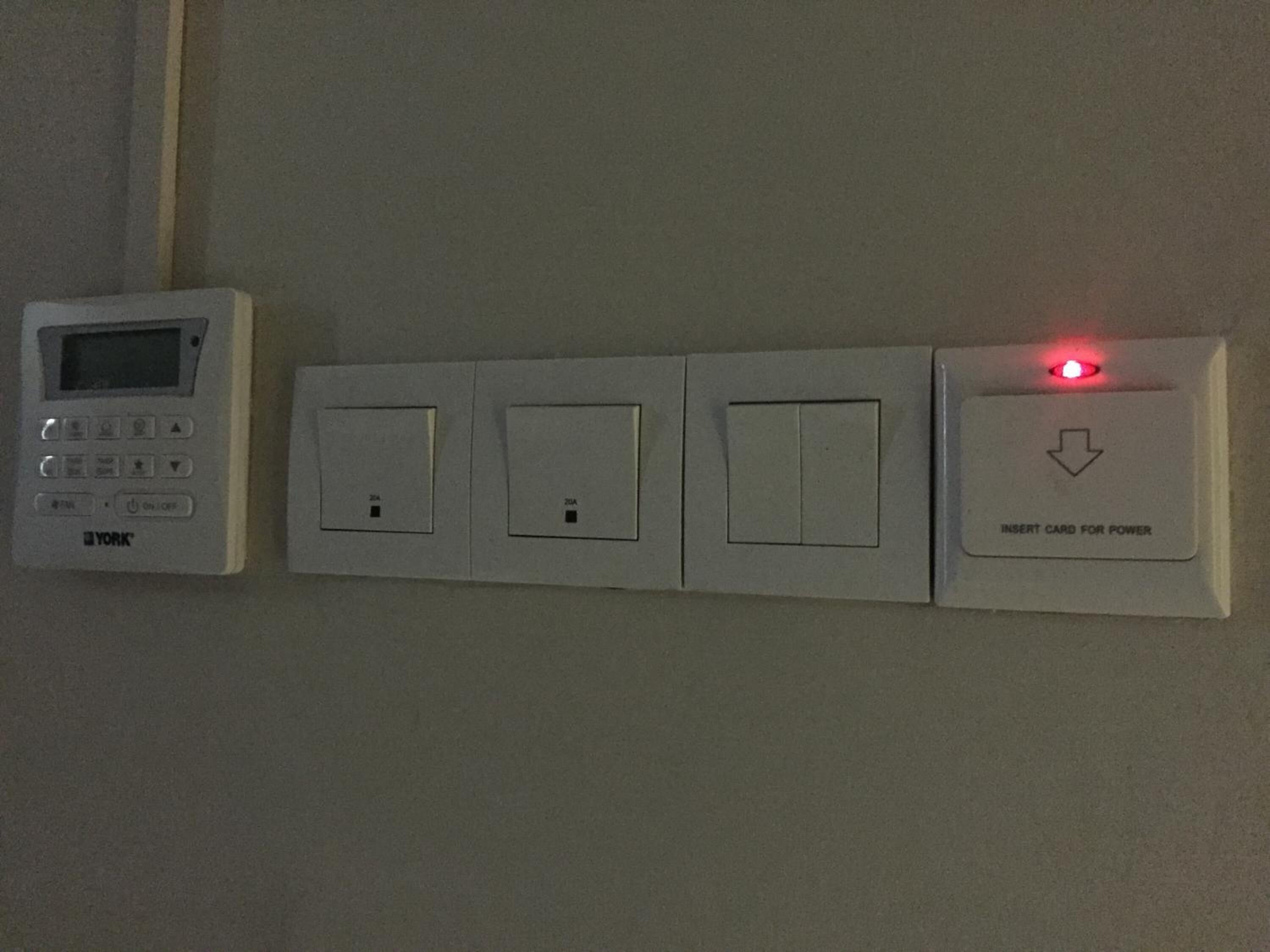 A wall-mounted control panel with a digital display and four switches, one of which has a red light indicating power insertion.