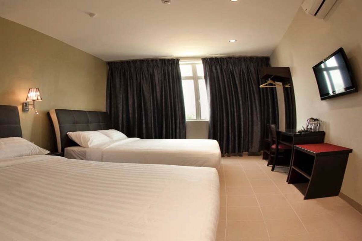 A hotel room with two beds, a desk, a TV, and a window with curtains.