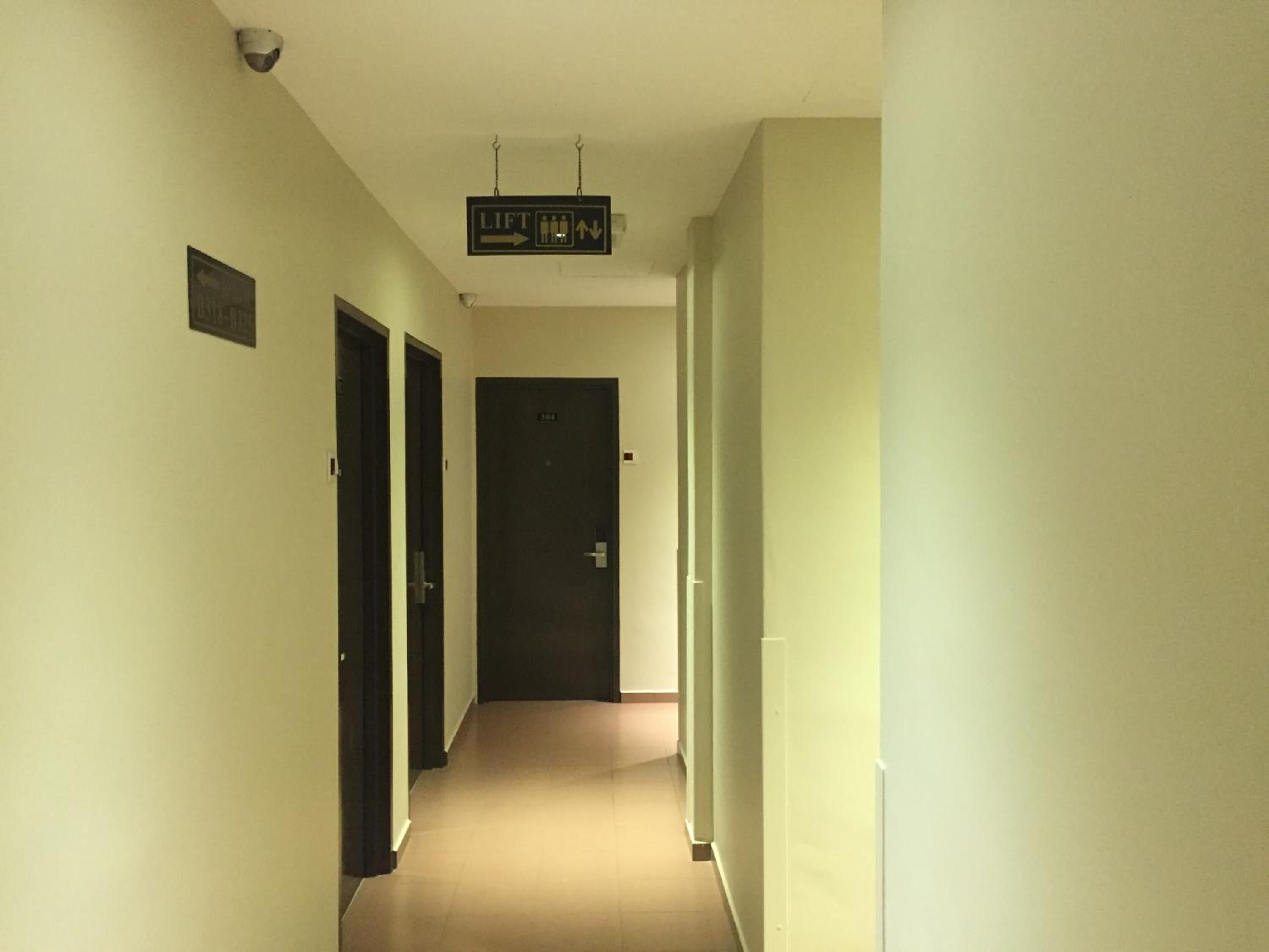 A narrow hallway with doors on both sides, a sign indicating a lift, and a security camera on the ceiling.
