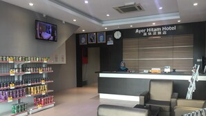 A hotel reception area with a reception desk, chairs, a clock, and shelves with products. - Ayer Hitam Hotel (Ayer Hitam)