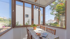 Un comedor iluminado por el sol, con una mesa dispuesta para dos, una planta en maceta y vistas al exterior.