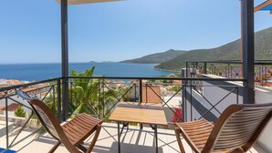 Un balcón con vista al mar, sillas de madera y una mesa.