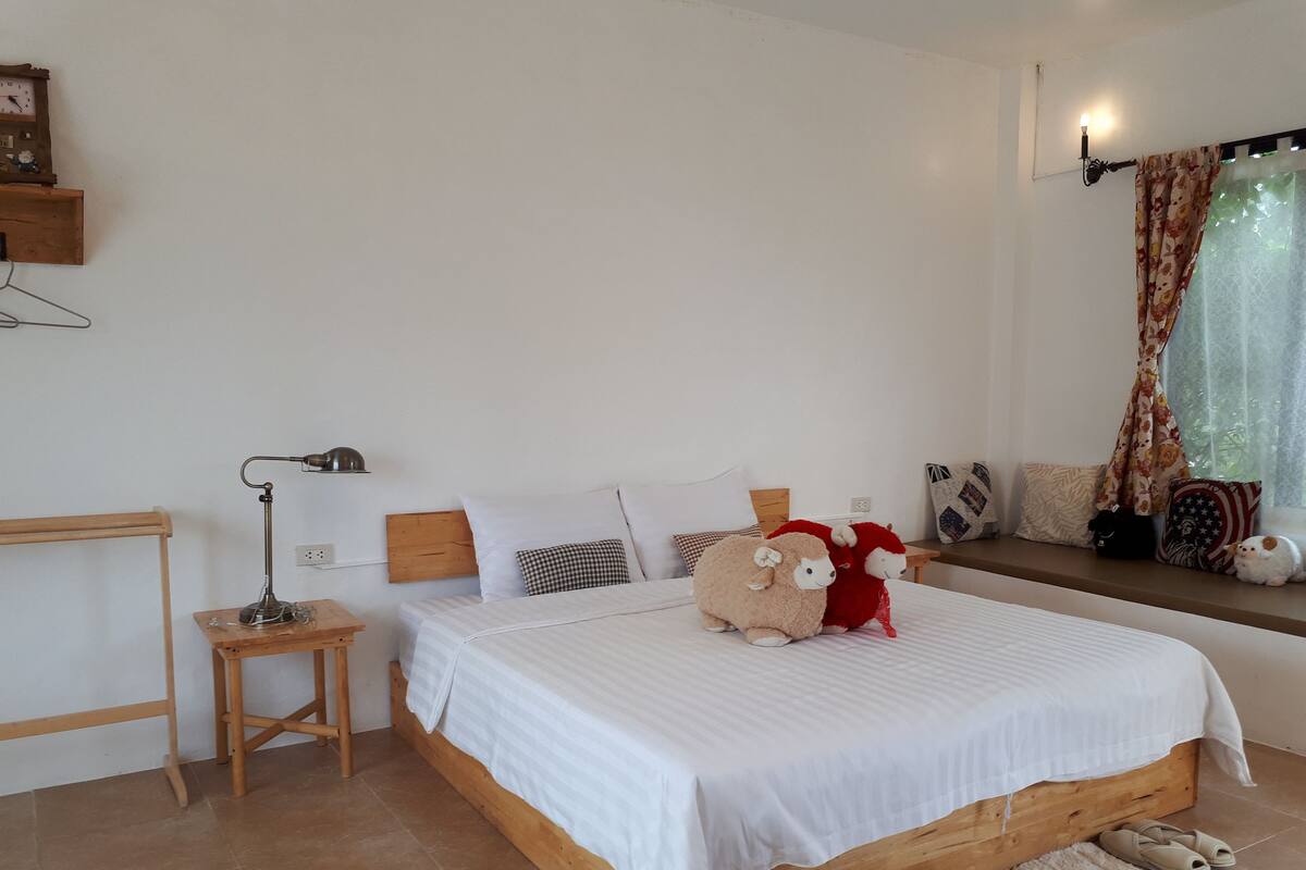 Une chambre à coucher avec un lit en bois, du linge de lit blanc, une lampe de chevet, une petite table de nuit en bois et une fenêtre avec des rideaux.