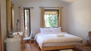 Un dormitorio con cama, una silla, una mesita y una ventana con cortinas.