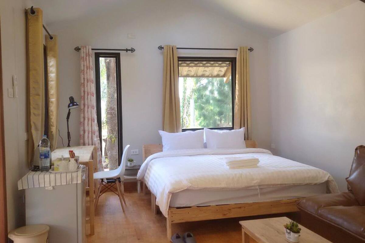 Une chambre à coucher avec un lit, une chaise, une petite table et une fenêtre avec des rideaux.