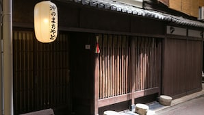 A traditional Japanese building with a wooden exterior, a hanging paper lantern, and a bench with a sign indicating it is a guesthouse. - Guesthouse OKI's Inn - Hostel (Kyoto)