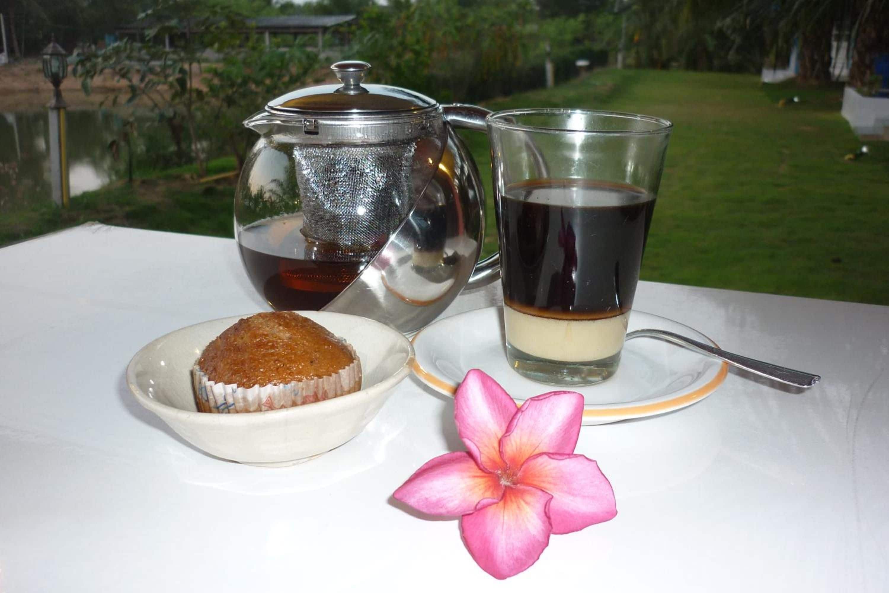 Una mesa con una tetera, una taza de té, un plato con un pastel y una flor.