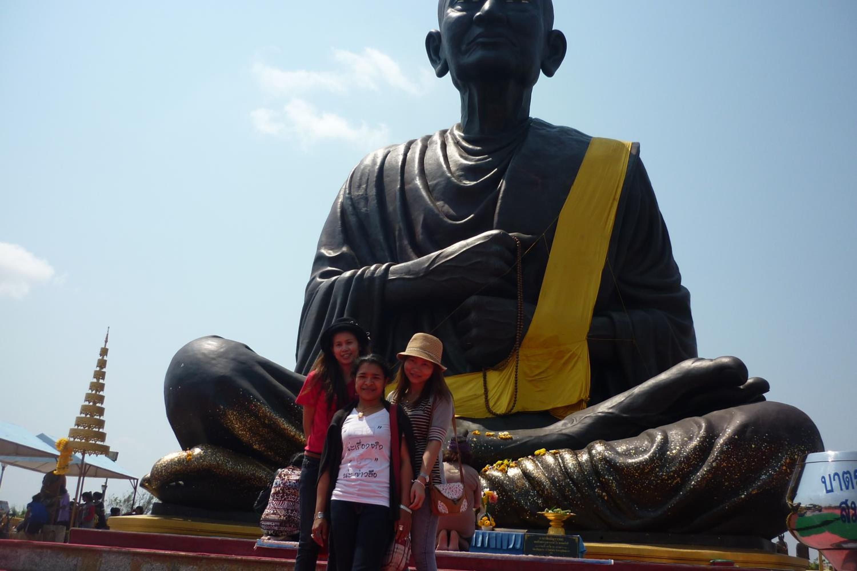 Una estatua grande de una figura sentada con un cinturón amarillo, rodeada por una multitud.