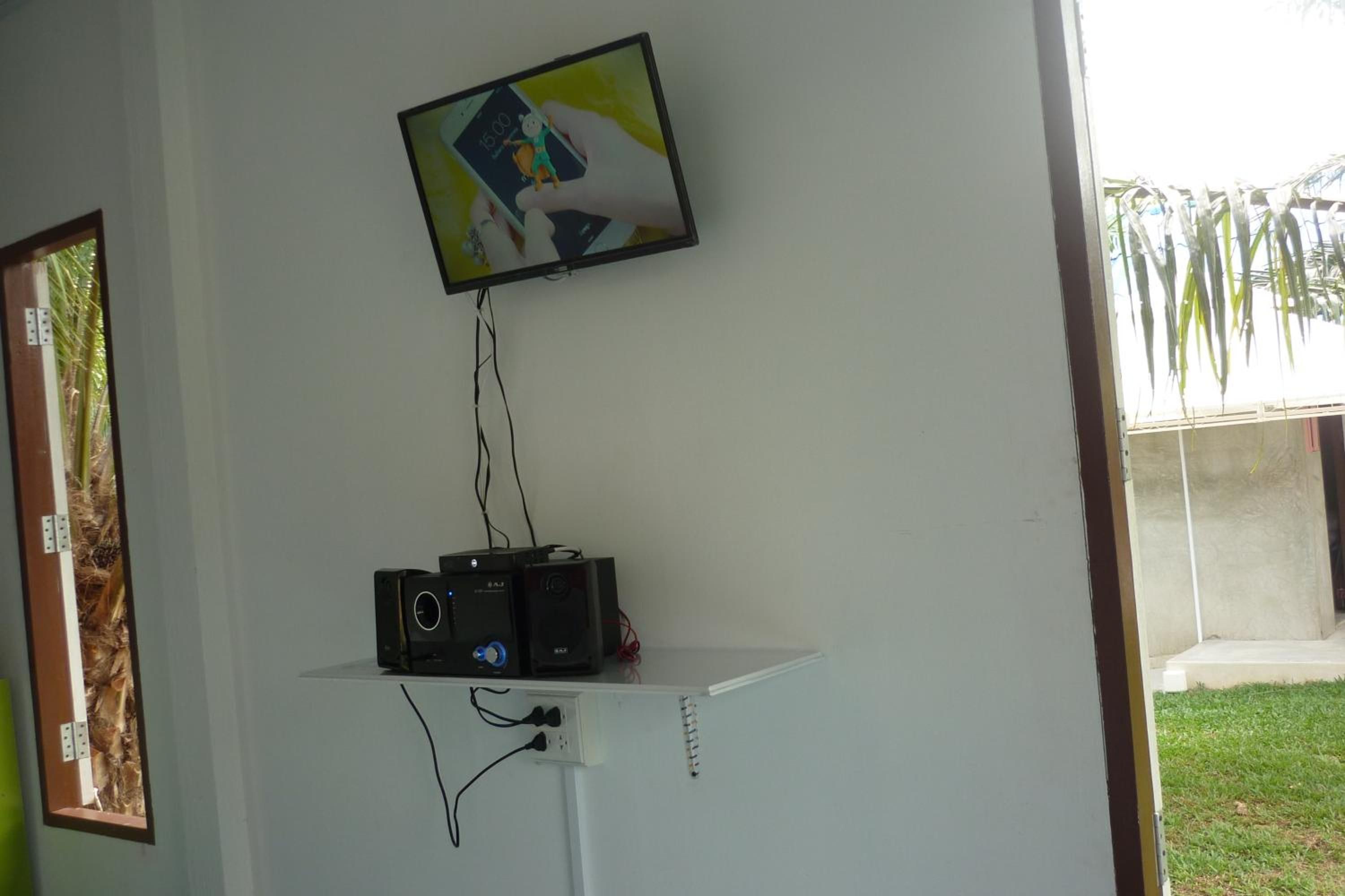 Una habitación con una televisión instalada en la pared, una mesita con equipo de sonido y un ventanal con vistas a zonas verdes.