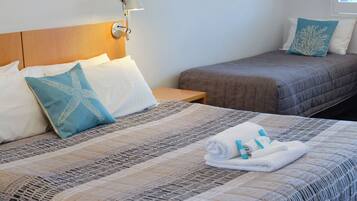 A hotel room with two beds, a nightstand, a lamp, and a window with blinds.