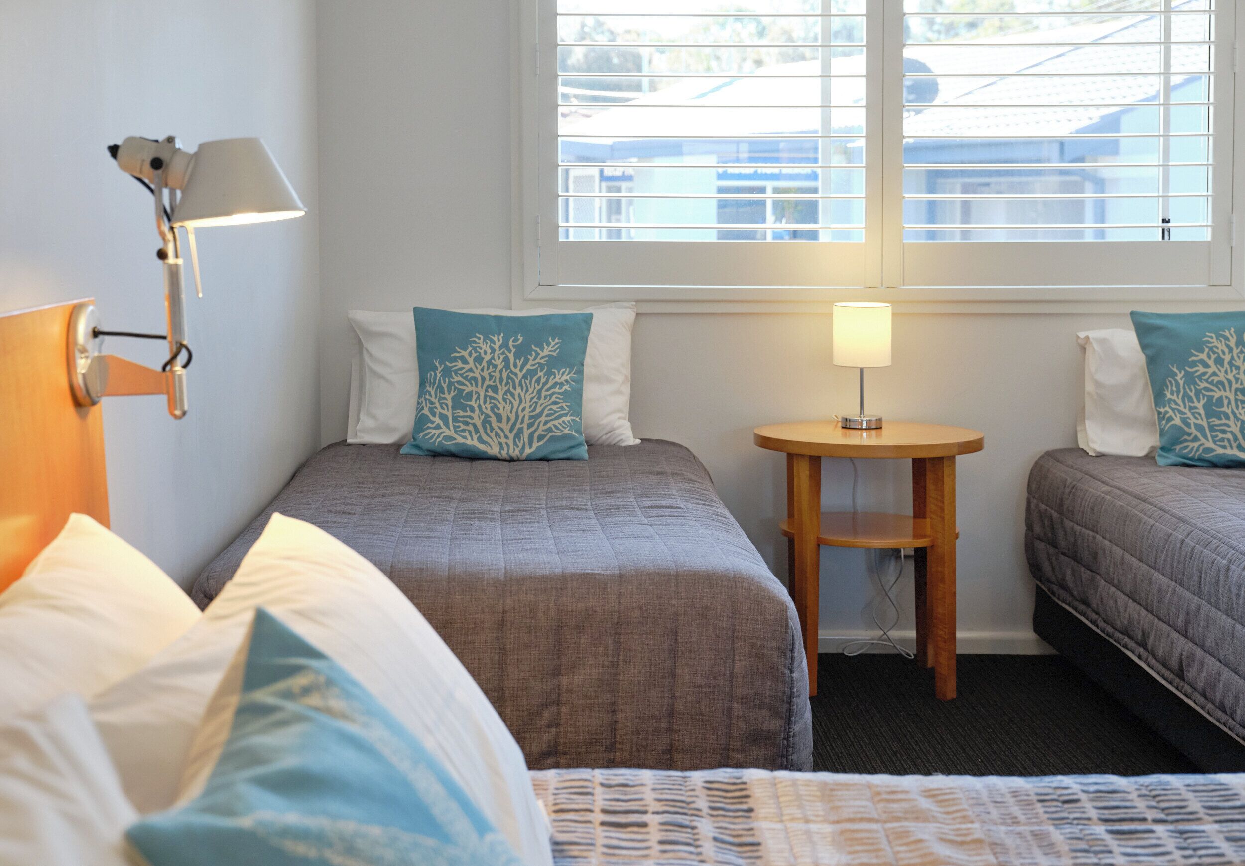Une chambre d’hôtel avec deux lits, une petite table et une fenêtre avec des stores.