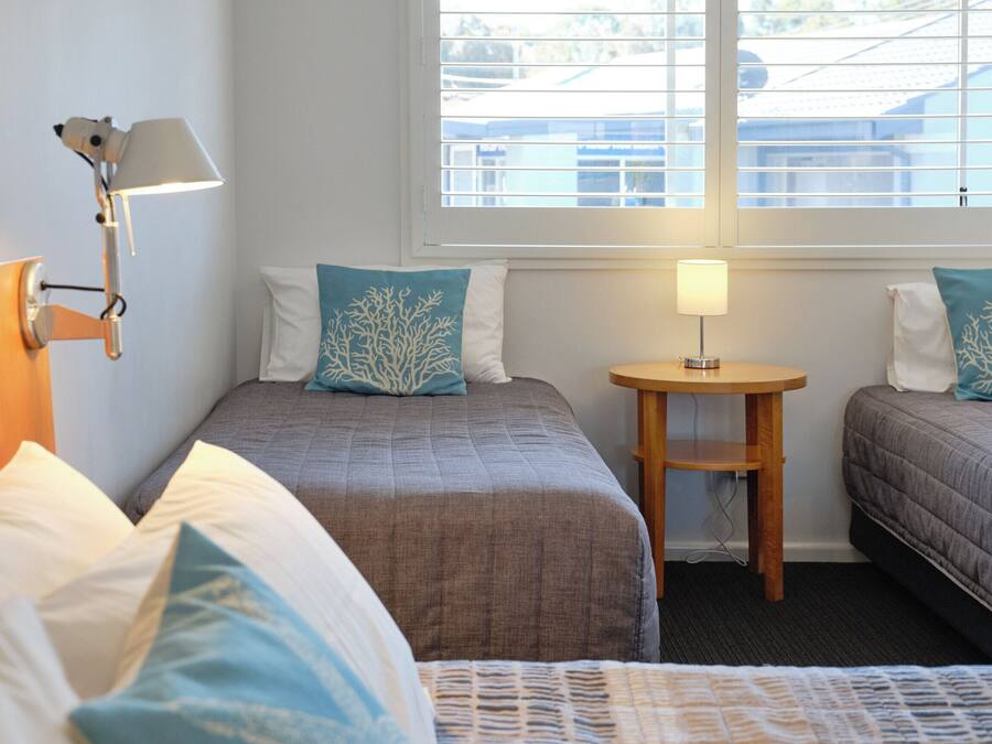 A hotel room with two beds, a small table, and a window with blinds.