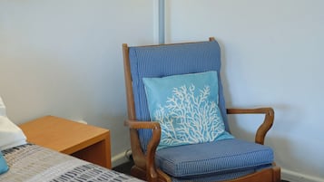 Ett hotellrum med en trästol med en blå kudde, ett sängbord och en lampa med en träbas.