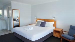 Habitación de hotel ordenada con una cama grande, mesitas de noche, una silla y un espejo.