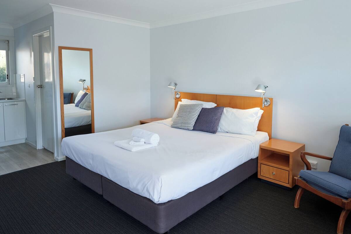 A neatly arranged hotel room with a large bed, bedside tables, a chair, and a mirror.
