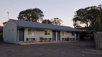 Um motel térreo com telhado de azulejos, área de estar coberta ao ar livre e estacionamento cercado.