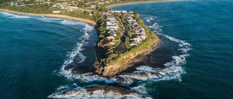 Vista aérea de una zona residencial costera con casas a lo largo de la línea de costa, rodeada de agua y vegetación.