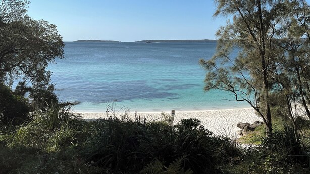 Una playa con agua turquesa cristalina, una orilla arenosa e islas a lo lejos.