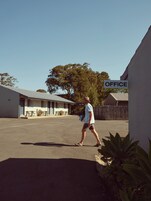 Un hombre caminando en un estacionamiento, con un edificio que dice 'OFFICE' al fondo.