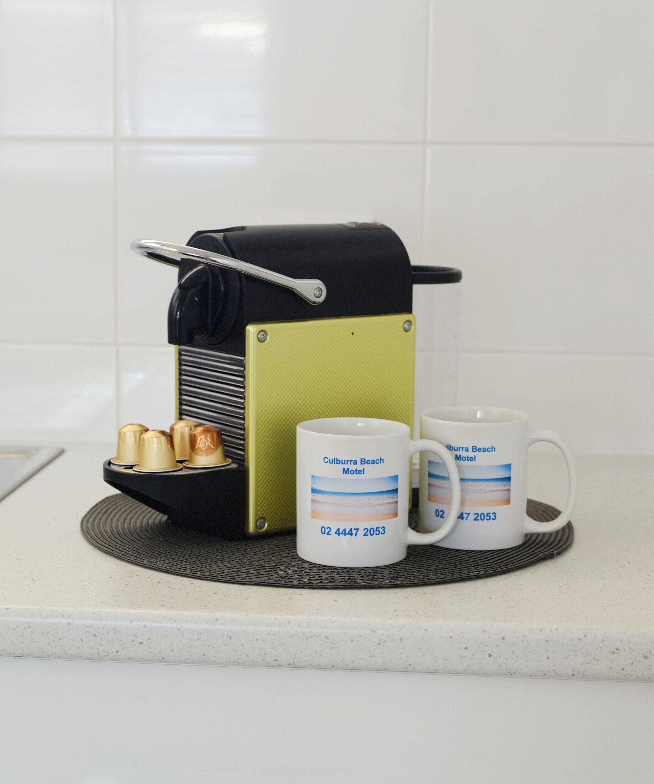 Une machine à café, deux tasses et une assiette avec trois sous-tasses sont posés sur un comptoir de cuisine.