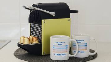 A coffee maker, two mugs, and a plate with three cups on a kitchen counter.