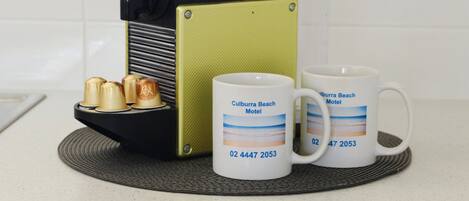 A coffee maker, two mugs, and a plate with three cups on a kitchen counter.