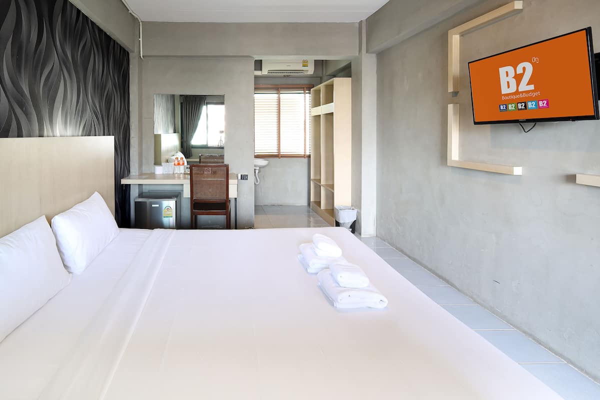 A hotel room with a large bed, a desk, a mirror, a sink, and a television displaying 'B2 Boutique&Budget'.