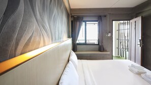 A hotel room with a bed, a bedside table with towels, a window with curtains, and a door with a number plate. - B2 Lanna Boutique & Budget Hotel (Chiang Mai)