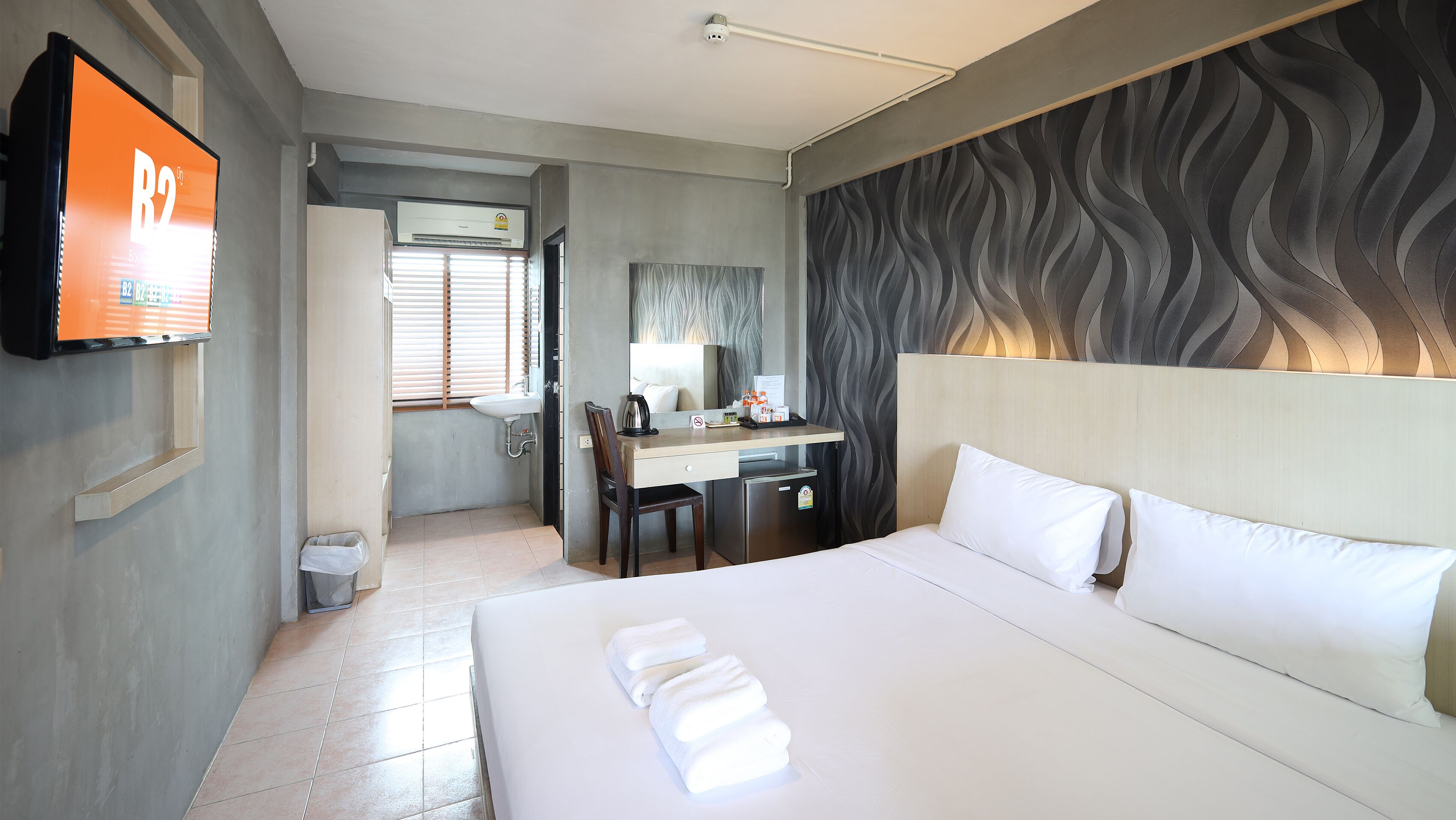A hotel room with a bed, a desk, a chair, a sink, and a television.