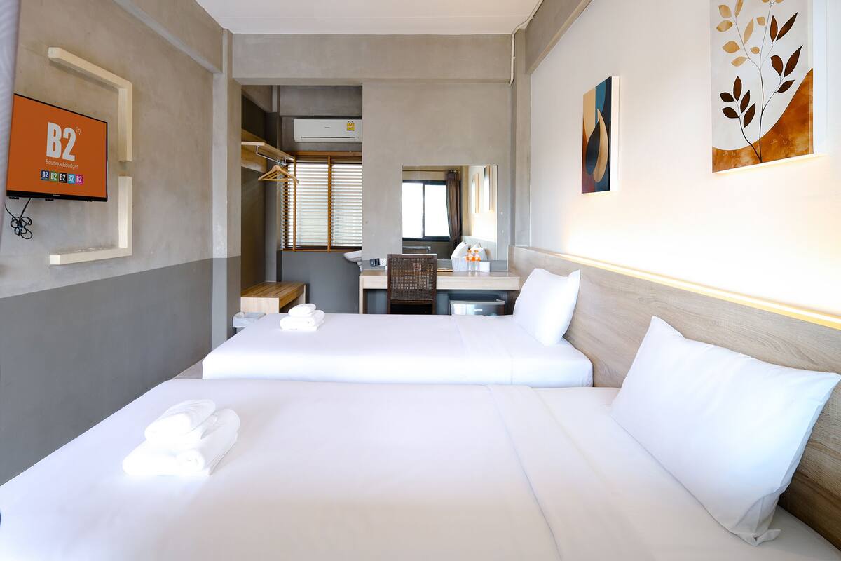 A hotel room with two beds, a desk, a chair, a mirror, and a TV displaying 'B2 Boutique & Budget'.
