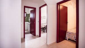 Um corredor com piso ladrilhado, um banheiro com parede verde e uma sala de jantar com mesa e cadeiras.
