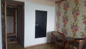 Una habitació amb una porta de fusta, una pissarra a la paret, paper pintat amb motius florals i una taula de fusta petita amb una cadira.