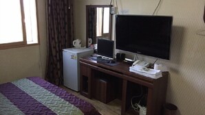 Habitació d'hotel amb un llit, una escriptori amb un ordinador, televisió, nevera i una finestra amb cortines.