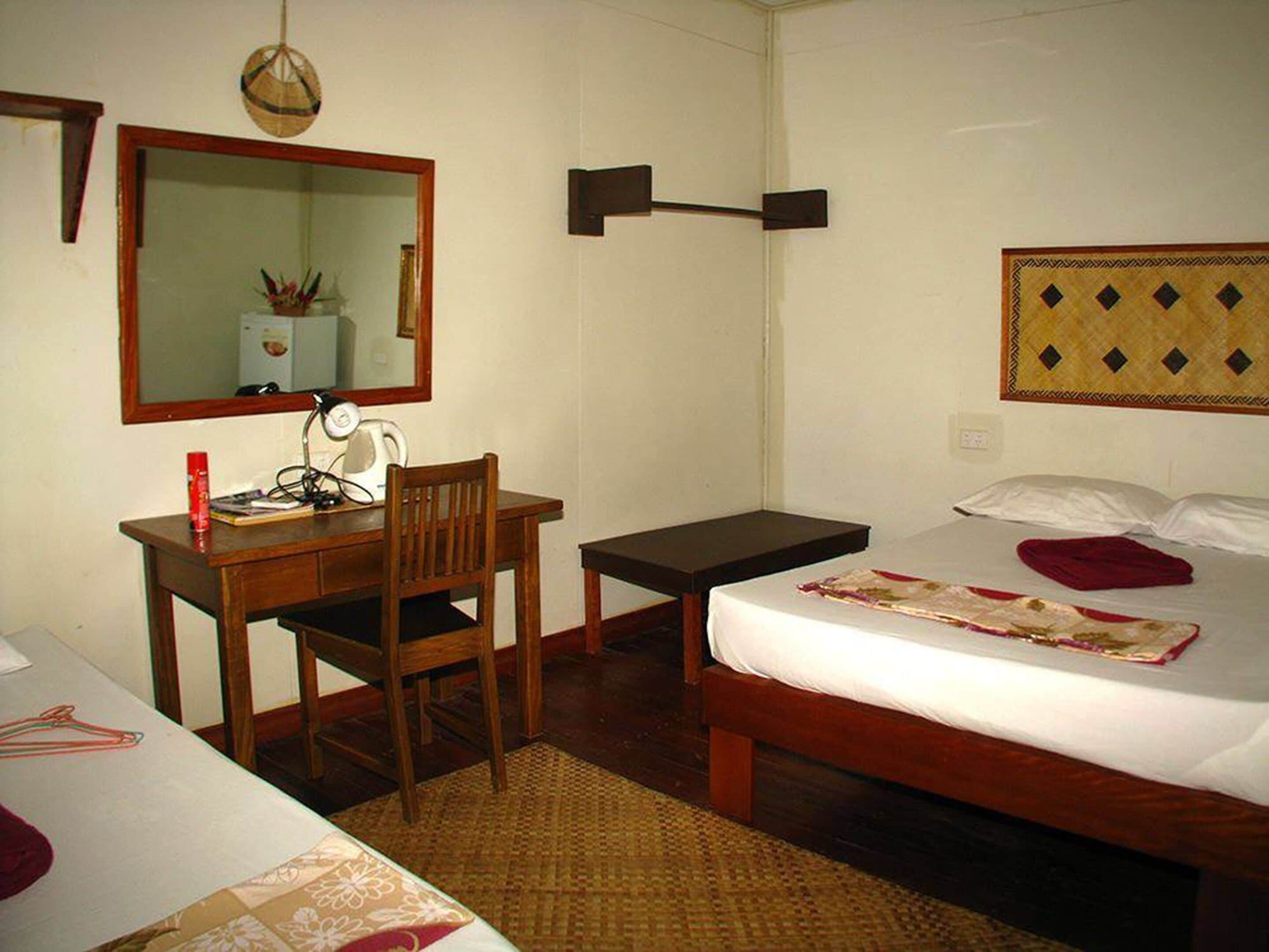 A room with a bed, a desk, a chair, a mirror, and a wall-mounted lamp.