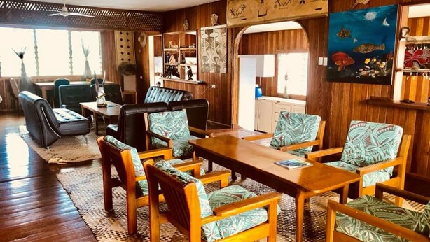 A spacious room with a wooden dining table surrounded by chairs, a ceiling fan, and a view of the kitchen through an archway. - Qua Roviana Motel (Munda)