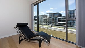 A modern room with a black lounge chair, large windows, and a view of modern buildings across a body of water. - Accommodate Canberra - Aurora (Kingston)