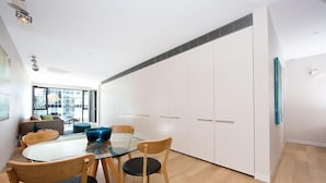 A modern kitchen with a glass dining table, wooden chairs, and white cabinets. - Accommodate Canberra - Aurora (Kingston)