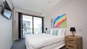 A modern hotel room with a large bed, a wooden nightstand, a colorful abstract painting, a flat-screen TV, and a sliding glass door leading to a balcony. - Accommodate Canberra - Aurora (Kingston)