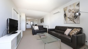 A modern living room with a flat-screen TV, leather sofas, a glass coffee table, and a large floral painting on the wall. - Accommodate Canberra - Aspire (Kingston)