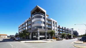 A multi-story building with balconies, a parking lot, and a clear sky. - Accommodate Canberra - Aspire (Kingston)