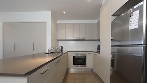 A modern kitchen with stainless steel appliances, white cabinetry, and a tiled floor. - Accommodate Canberra - Aspire (Kingston)